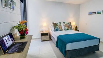 A modern hotel room with a bed, bedside lamps, a laptop on a desk, and a potted plant.