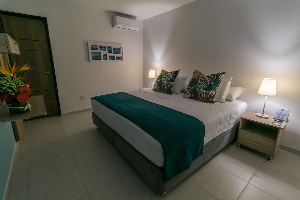 Un dormitorio ordenado con cama, mesitas de noche, aire acondicionado instalado en la pared y un cuadro enmarcado.