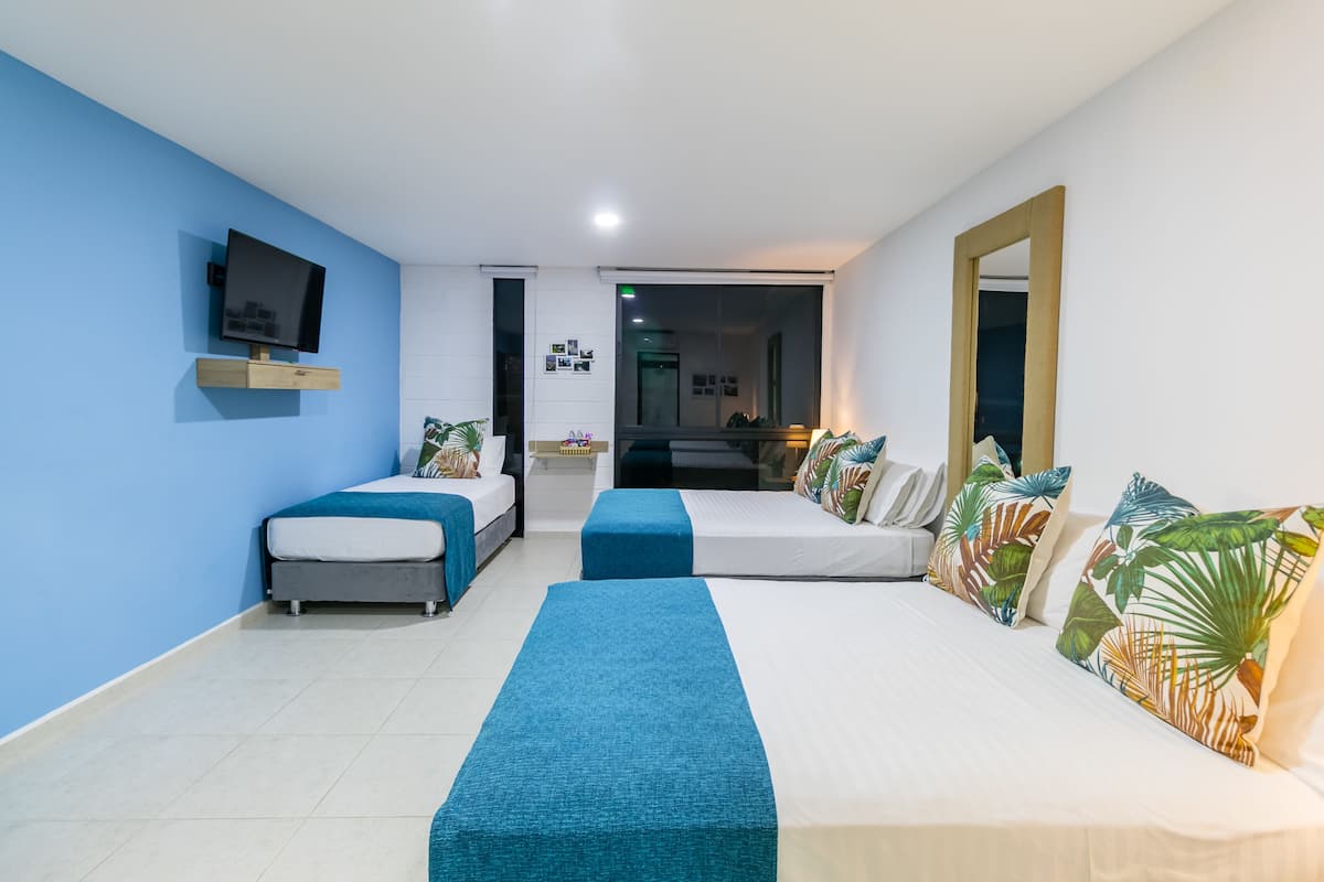 Una habitación de hotel con dos camas, televisión, espejo y un escritorio pequeño.