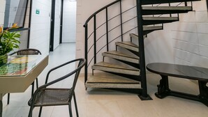 Una escalera de caracol con barandilla de metal, una mesa con sillas y una planta en maceta.