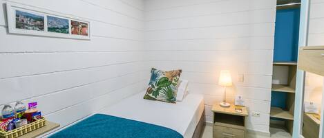 A small, neatly arranged bedroom with a bed, a nightstand, a lamp, and a shelf with toiletries.