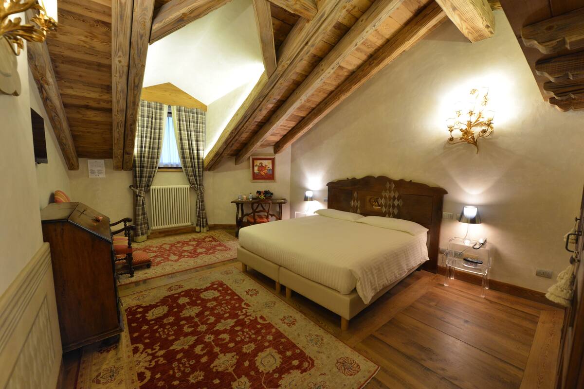 A bedroom with a wooden ceiling, a bed, a nightstand, a lamp, and a radiator.