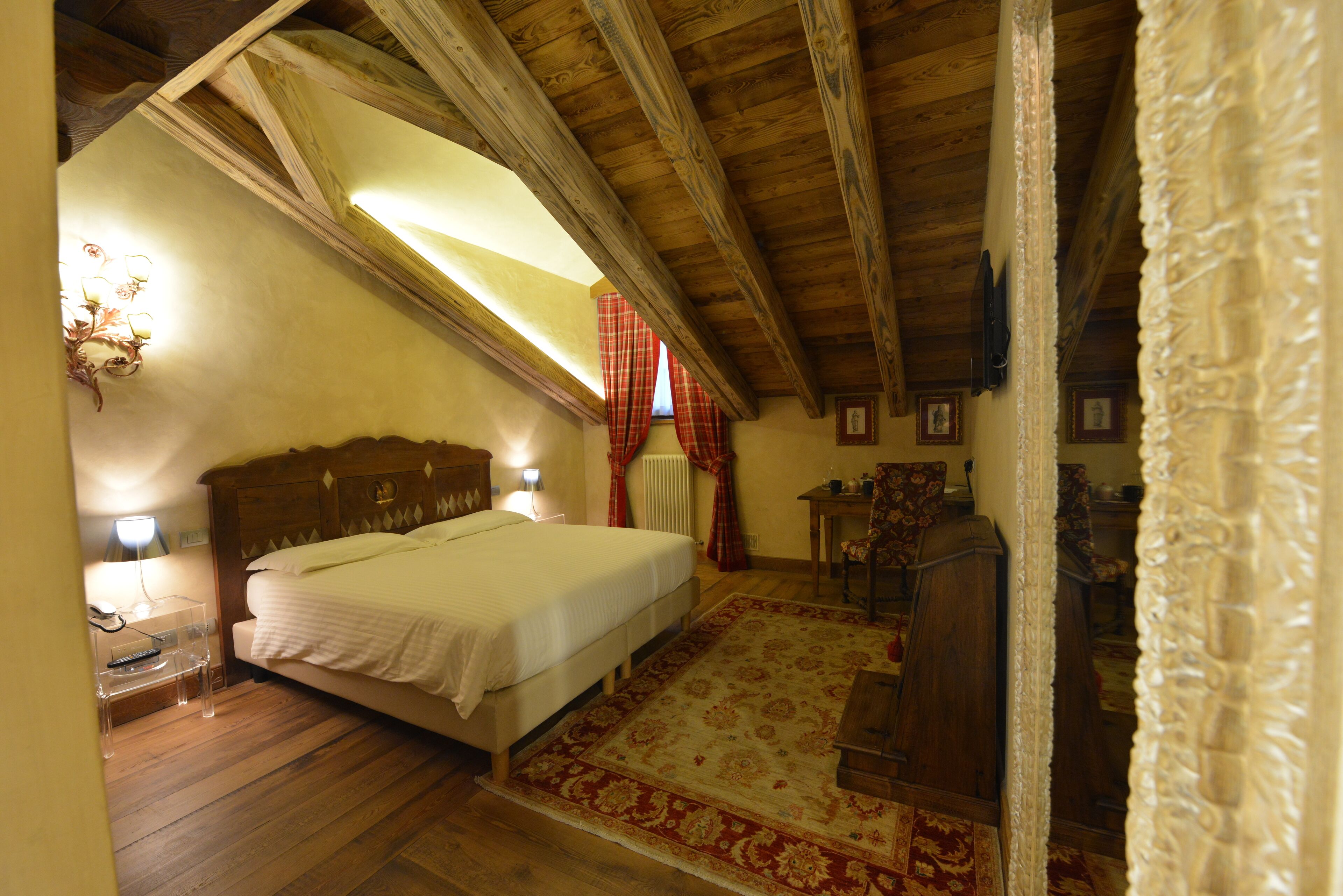 A bedroom with a wooden ceiling, a bed, a nightstand, a lamp, a chair, and a table.
