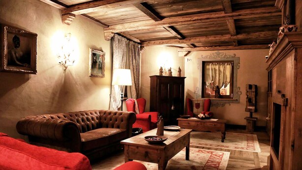 A cozy living room with a brown leather sofa, a red armchair, and a wooden coffee table. There is a wooden cabinet and a mirror on the wall. - Le Reve Charmant (Aosta)