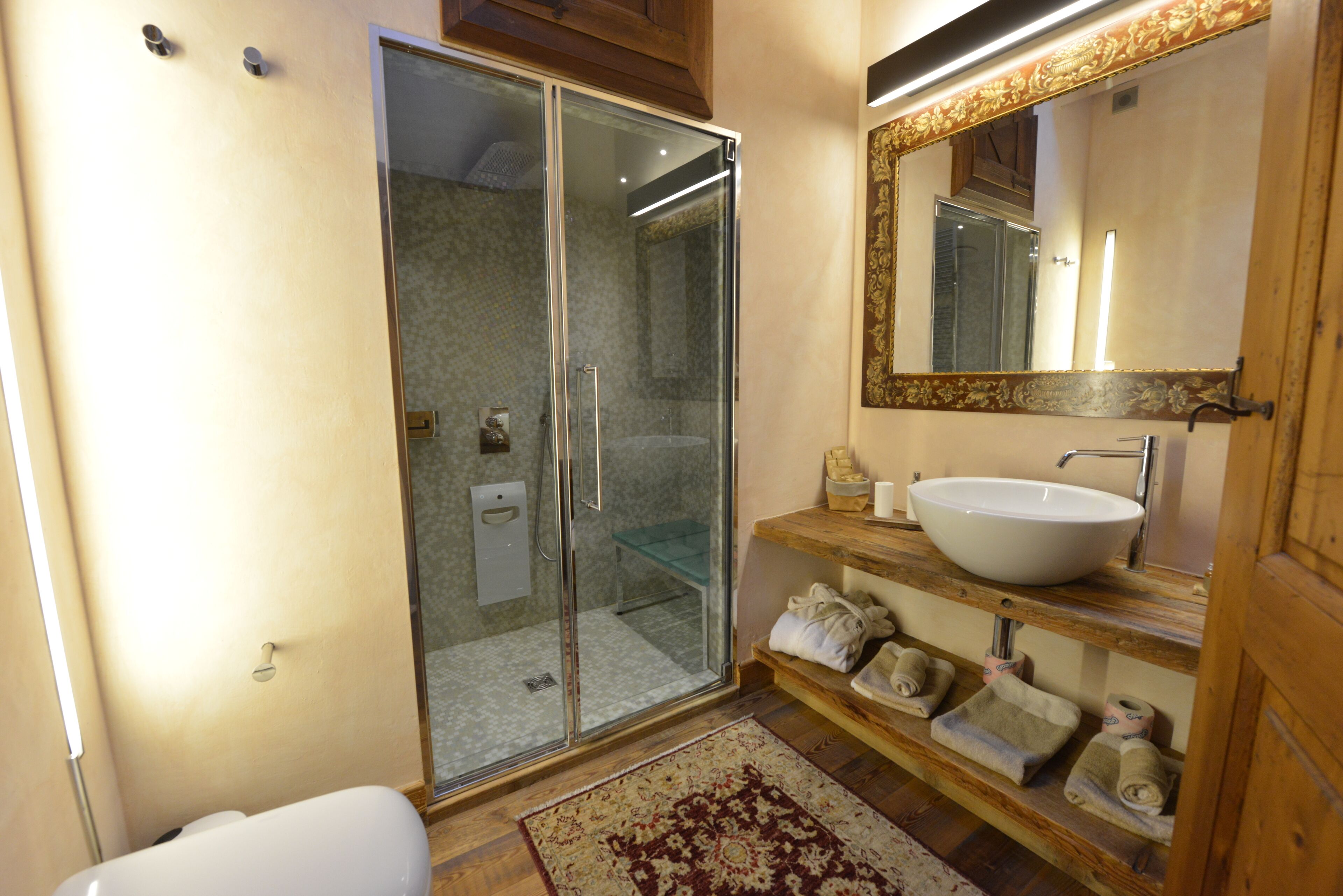 Une salle de bain avec une douche à parois de verre, un lavabo blanc et un meuble-lavabo en bois avec des serviettes.