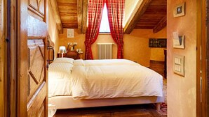 A wooden room with a bed, a window with red curtains, and a sloped ceiling. - Le Reve Charmant (Aosta)