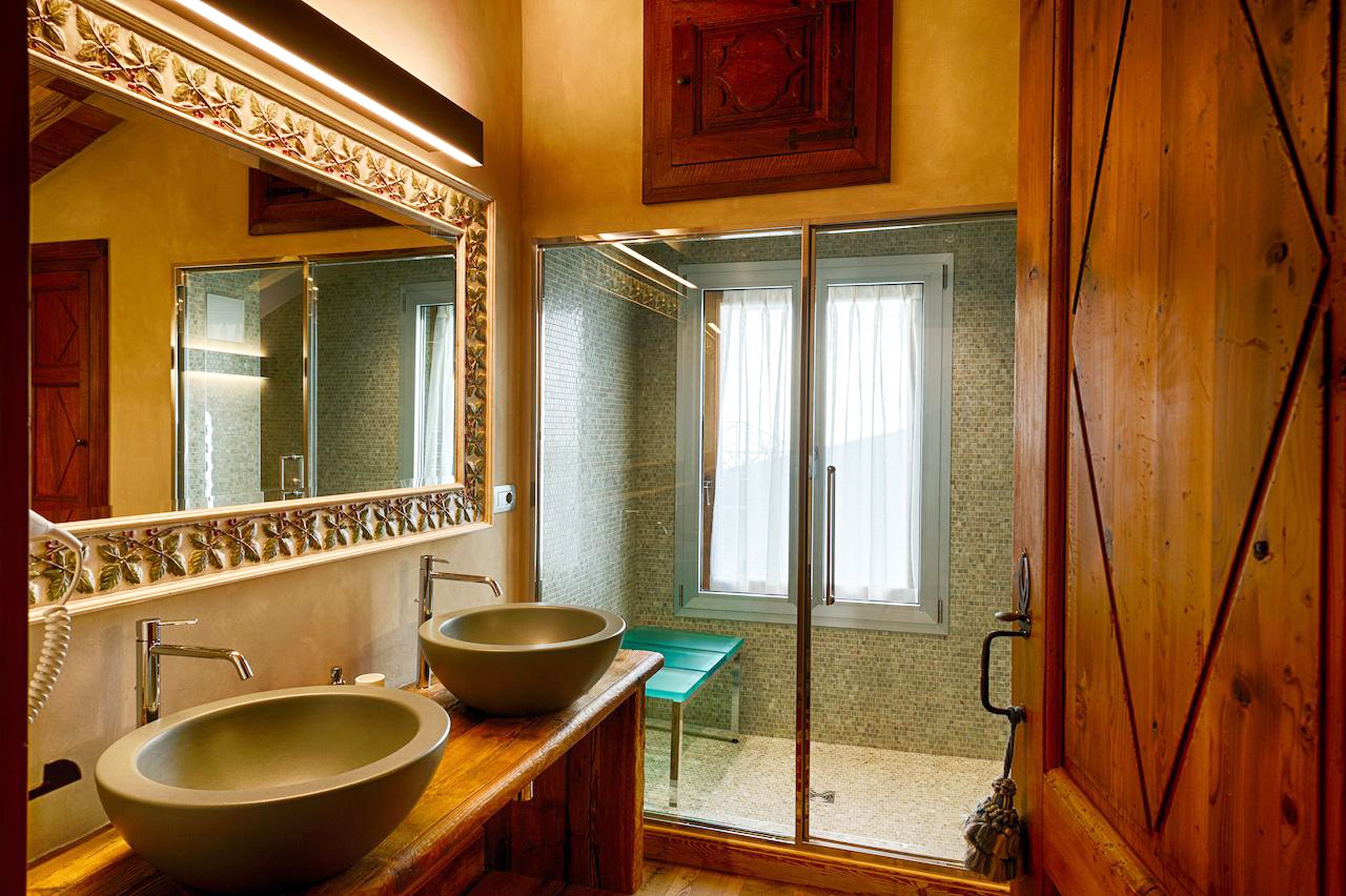 A bathroom with two large vessel sinks, a wooden vanity, a glass shower enclosure, and a view of the outside through a window.