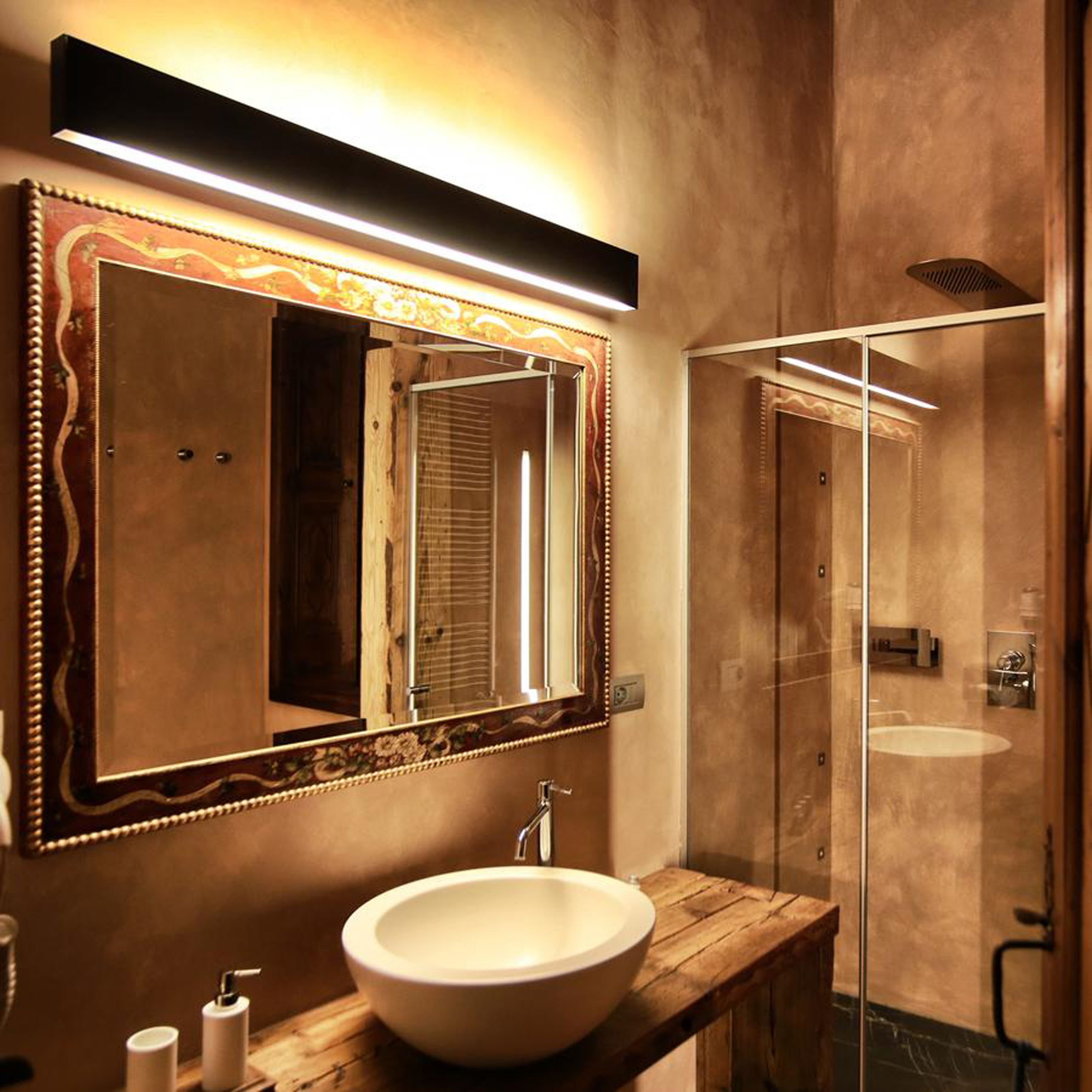 A bathroom with a large mirror, a wooden vanity, a white sink, and a glass shower enclosure.