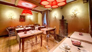 A dining area with wooden tables and chairs, red pendant lights, and wall sconces. - Le Reve Charmant (Aosta)