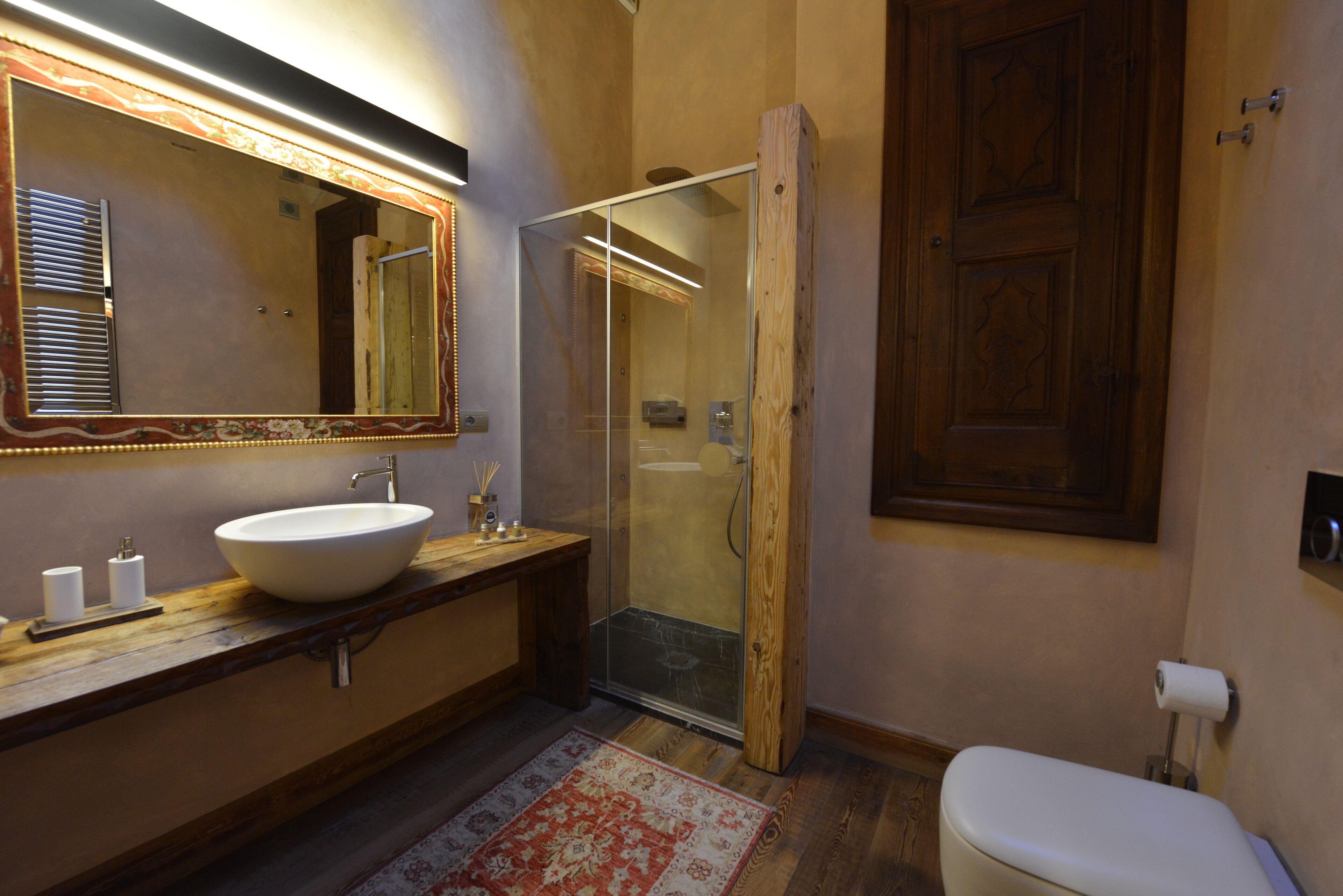 Een badkamer met een houten wastafelmeubel, een grote spiegel, een douchecabine met glazen wanden en een toilet.