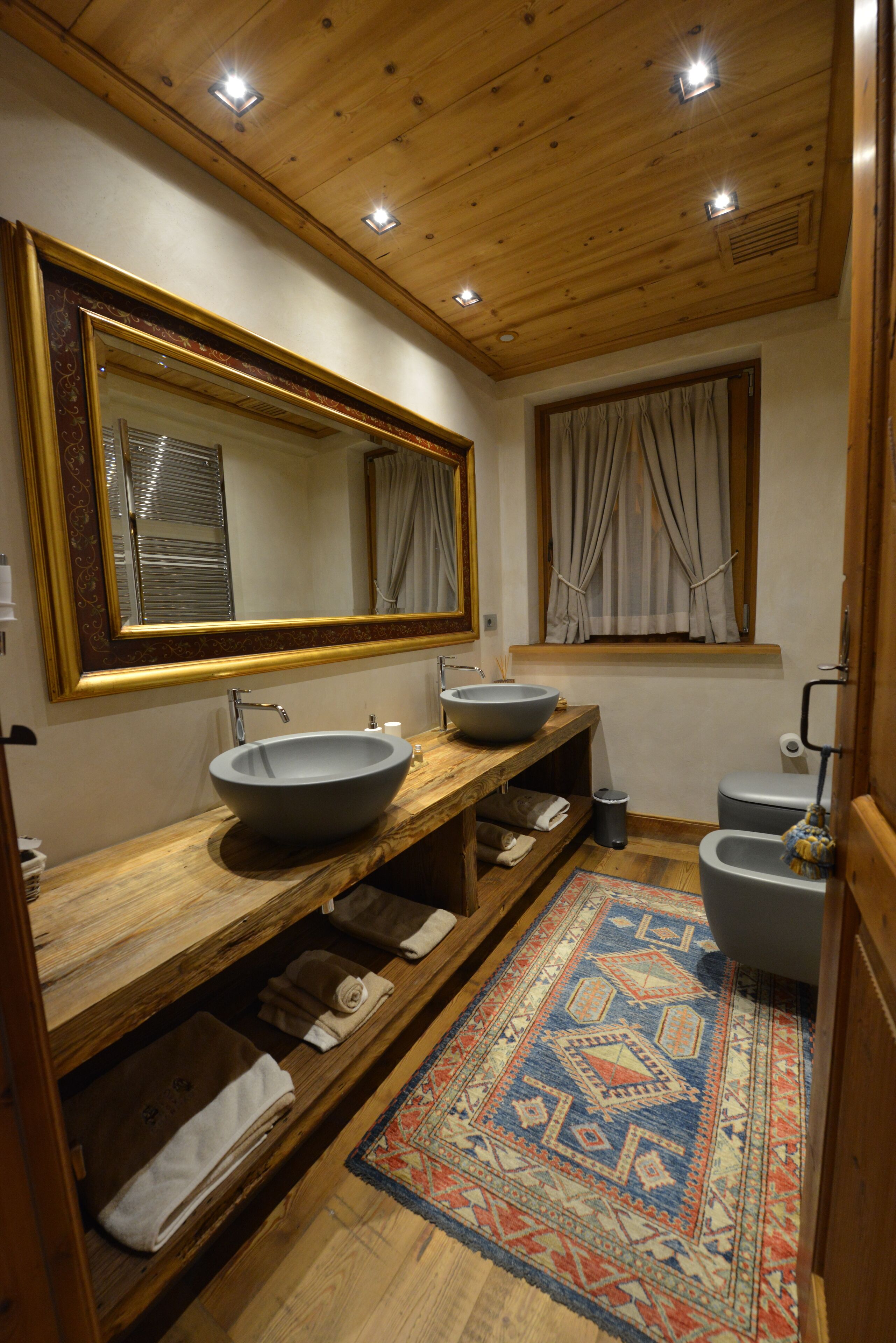 Ein Badezimmer mit einem Holzkosmetikschrank, einem großen Spiegel, einem Aufsatzbecken, einer Toilette und einem gemusterten Teppich.