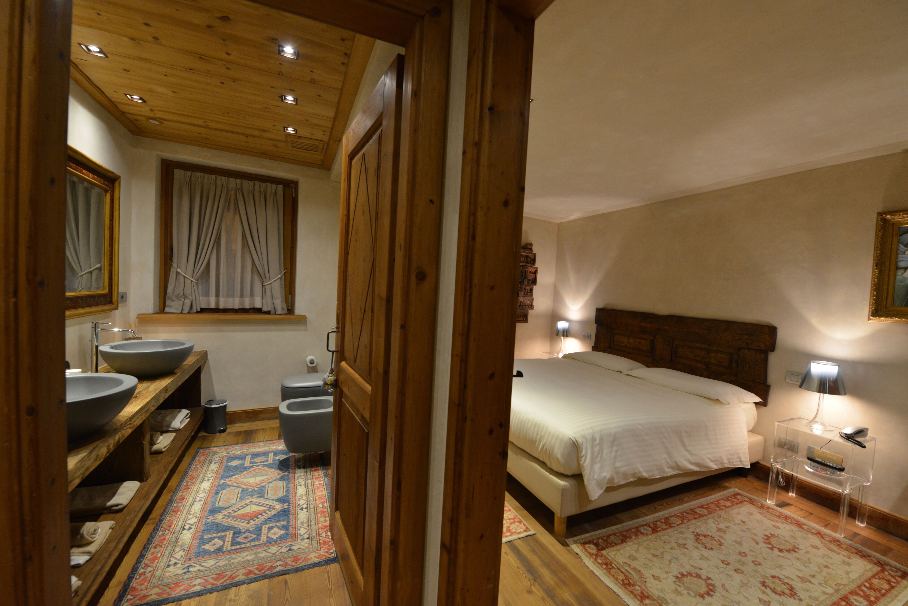 A bedroom with a wooden headboard, a large bed, a bedside table, a nightstand, and a window with curtains.