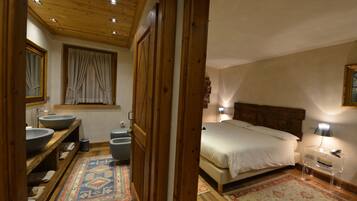A bedroom with a wooden headboard, a large bed, a bedside table, a nightstand, and a window with curtains.