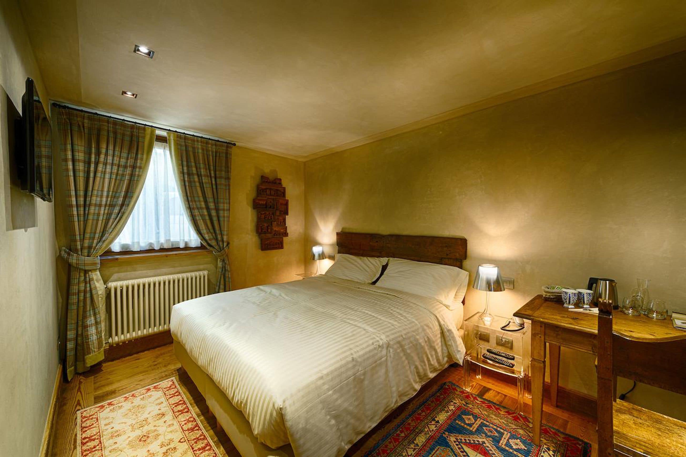 Een slaapkamer met een bed, een nachtkastje, een lamp, een radiator en een raam met gordijnen.