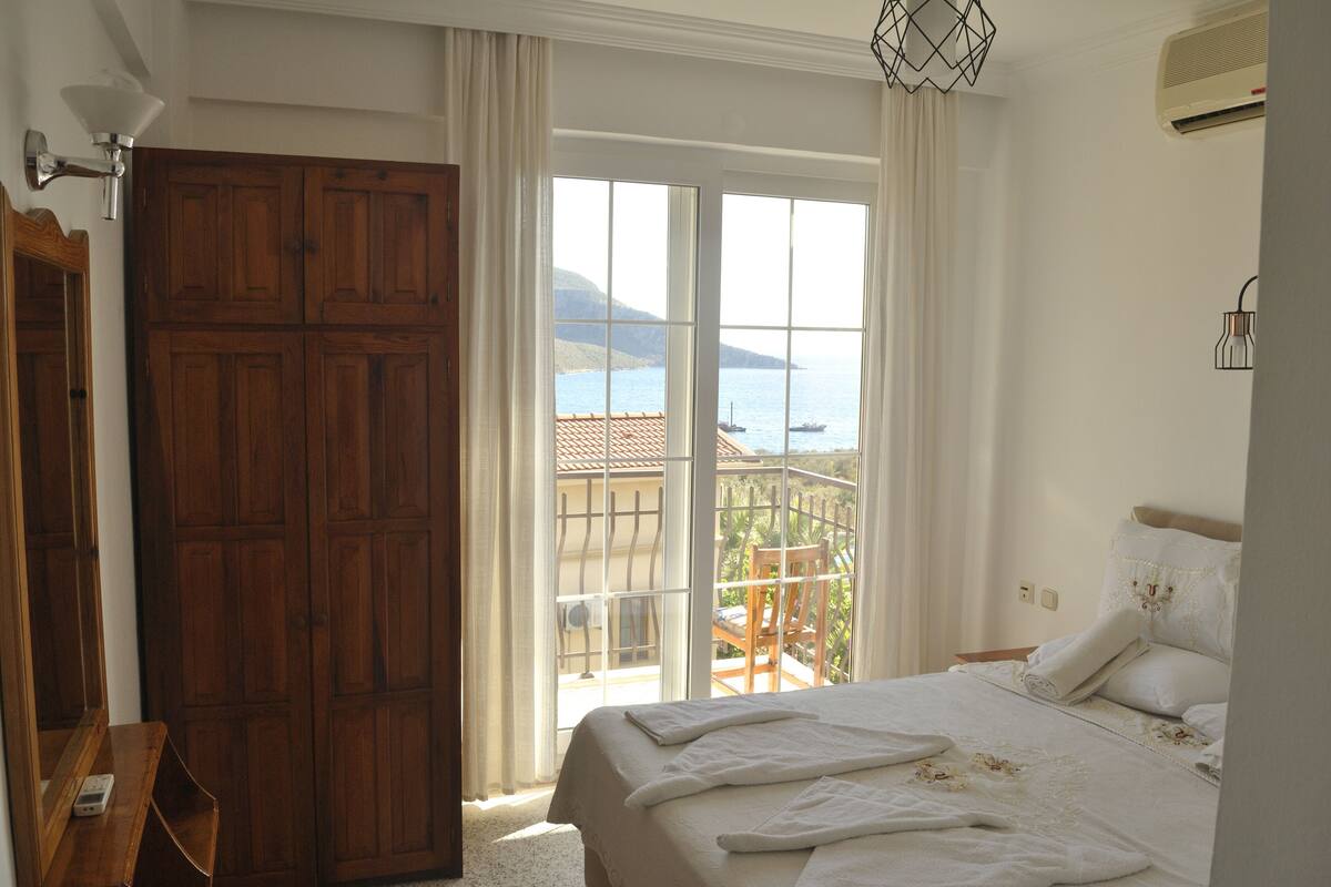 Un dormitorio con una cama grande, un armario de madera y un balcón con vista al mar.