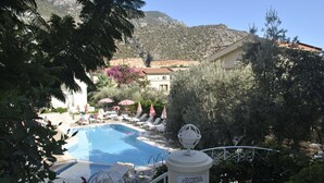 A pool area with lounge chairs and umbrellas, surrounded by greenery and a mountain backdrop. - Hotel Dionysia (Kas)