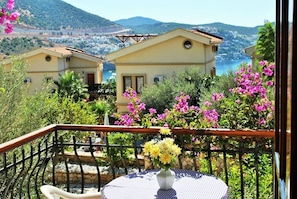 A balcony with a table and chairs, overlooking a coastal area with houses and a view of the sea. - Hotel Dionysia (Kas)