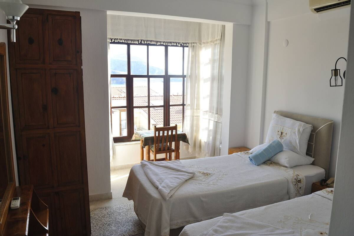 Un dormitorio con dos camas, un armario de madera y vistas al exterior a través de una ventana.