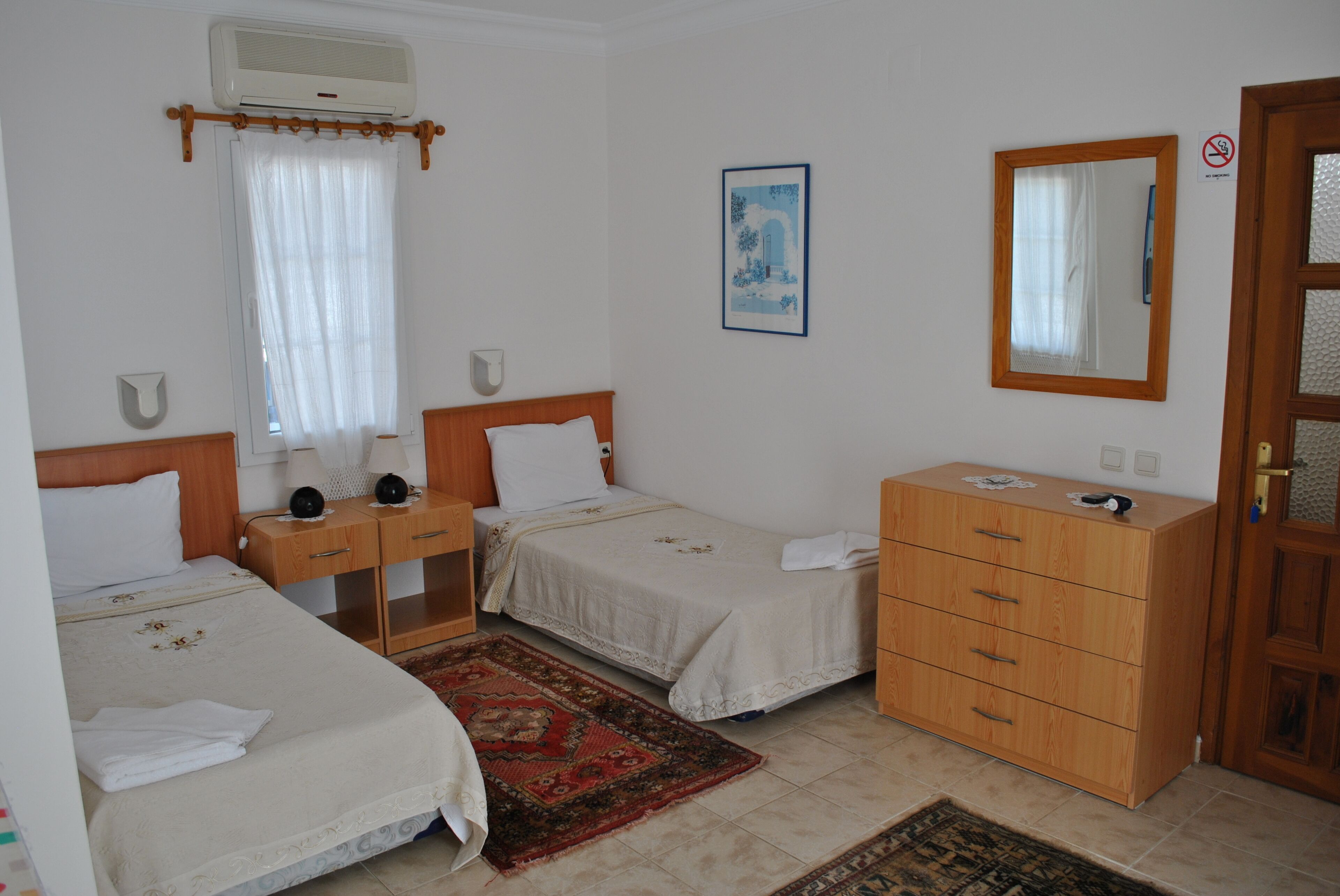 A hotel room with two single beds, a wooden dresser, a mirror, and a window with a curtain.