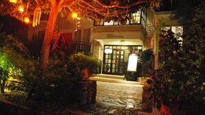 A hotel entrance with a stone-paved pathway leading to the door, surrounded by potted plants and a tree with hanging lights. - Hotel Dionysia (Kas)