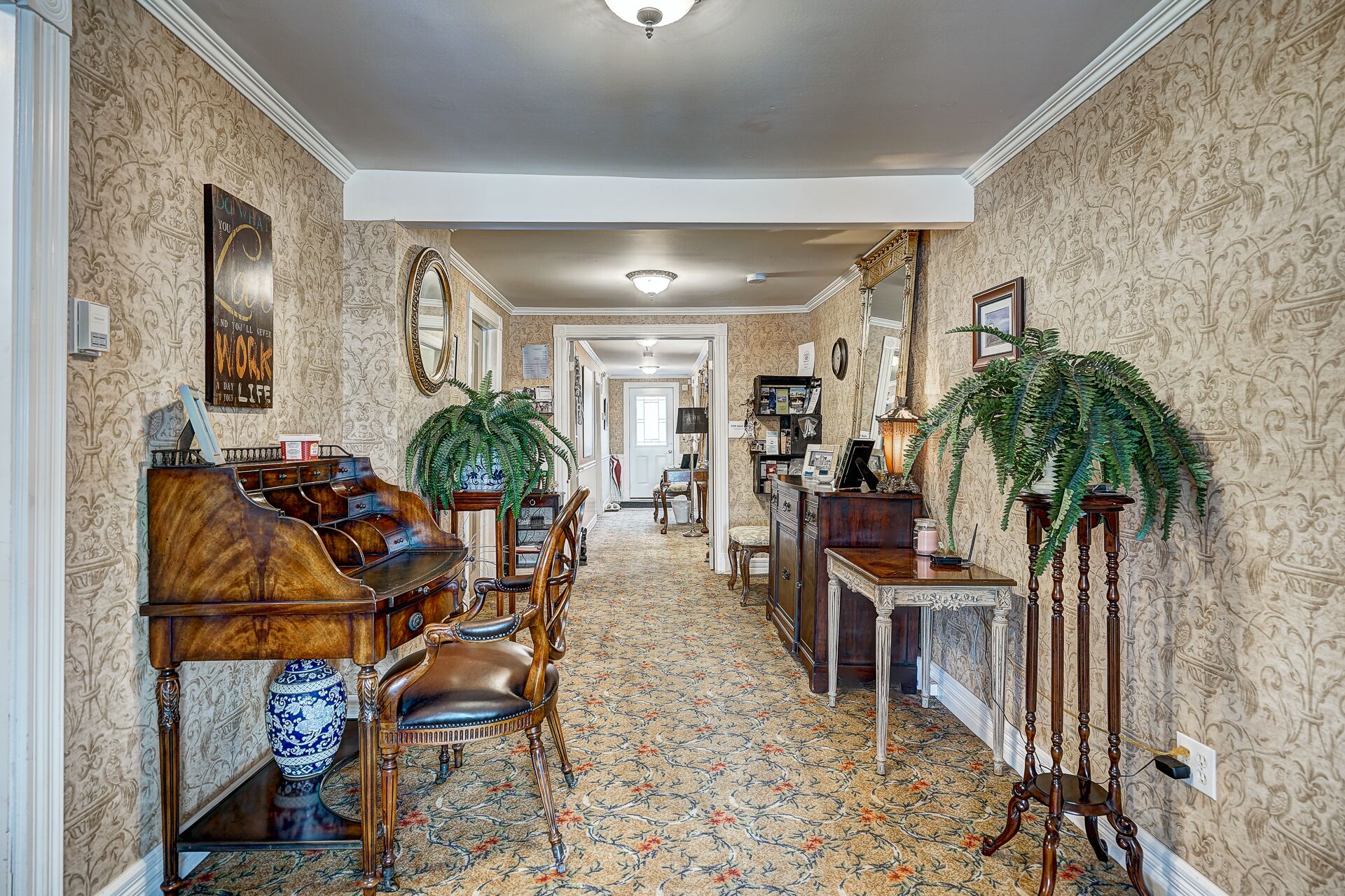 A hallway with a grand piano, a large fern plant, and a desk with a lamp.