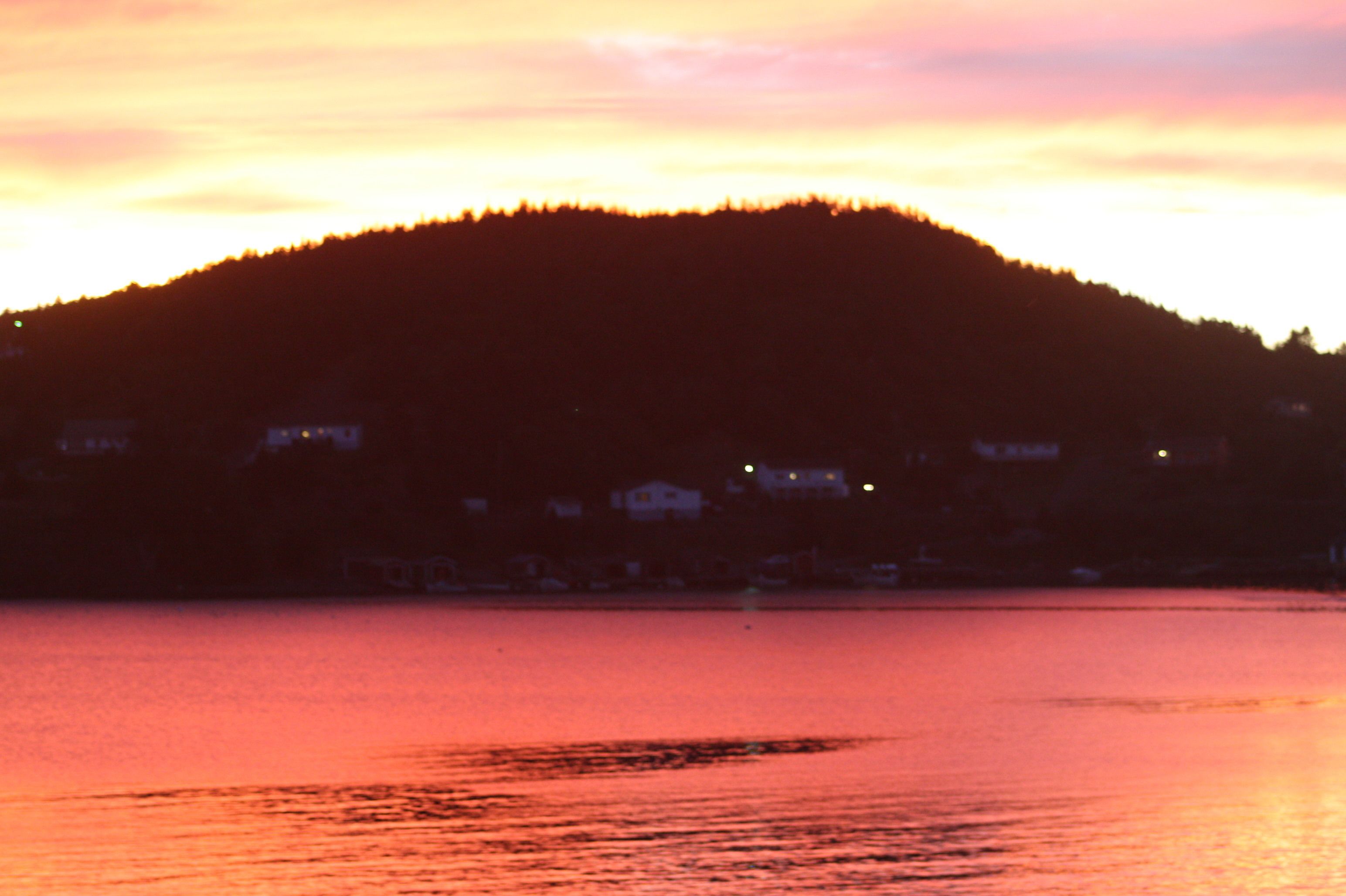A sunset over a body of water with a hill in the background.