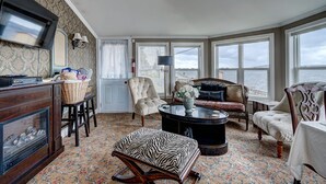 A cozy room with a large window overlooking the sea, a comfortable sofa, a wooden cabinet, and a zebra-patterned ottoman. - Inn By The Bay (Dildo)
