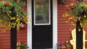 A red house with a black door, two hanging flower baskets, and a yellow chair outside. - Inn By The Bay (Dildo)