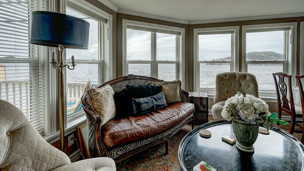 A cozy room with a leather sofa, a round table, and a view of the water through large windows. - Inn By The Bay (Dildo)