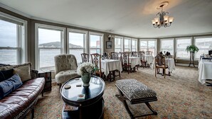 A spacious room with a large window overlooking a body of water, a round table with a vase of flowers, a zebra-patterned ottoman, and a leather sofa. - Inn By The Bay (Dildo)