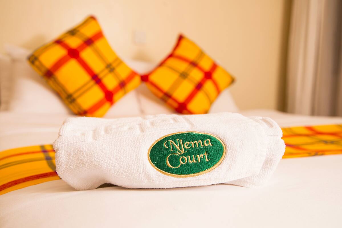 A neatly made bed with a white towel rolled up and a pillow with a plaid pattern.