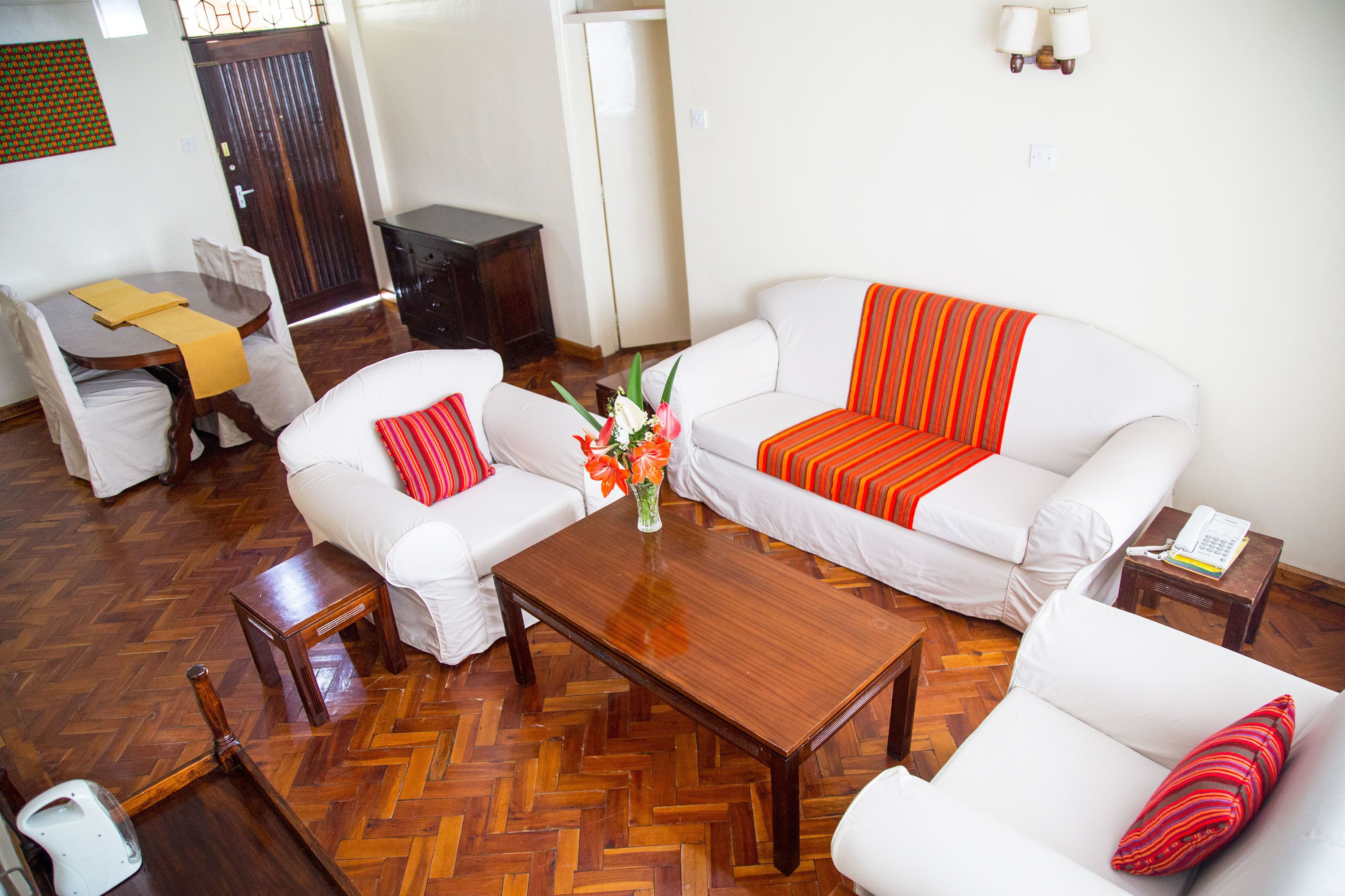 Una sala de estar con piso de madera en diseño espiga, sofás blancos con cojines a rayas, una mesa de centro de madera y una mesita auxiliar con un teléfono.