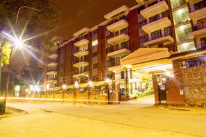 A multi-story hotel with balconies, a stone facade, and a well-lit entrance. - Njema Court Apartments (Nairobi)