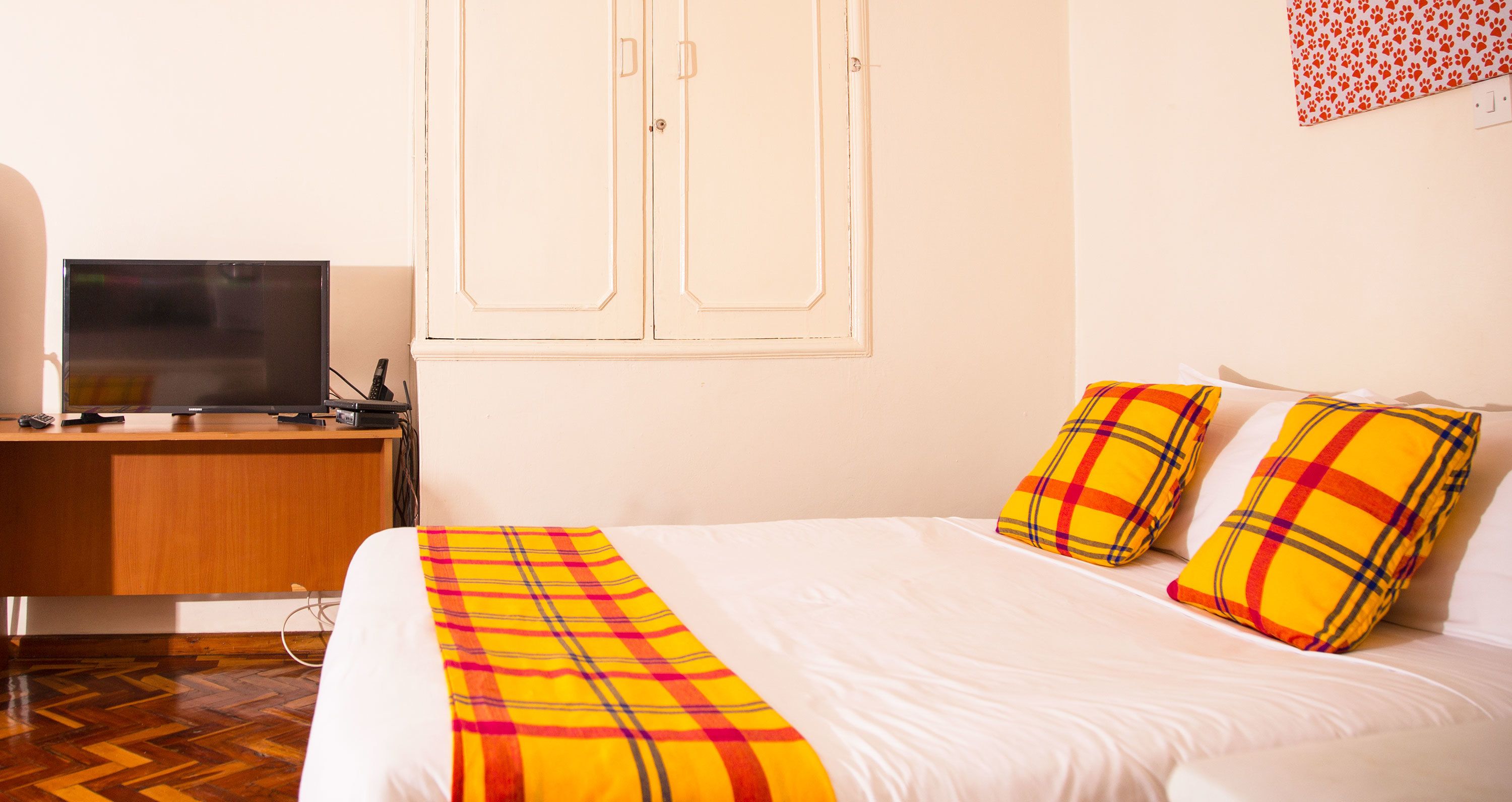 A hotel room with a bed, a desk with a television, and a wardrobe.