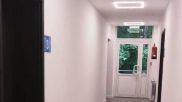 Un couloir avec un plancher en bois, des murs blancs et une porte sur le côté gauche. Un panneau indiquant le numéro 3 est fixé au mur.