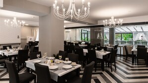 Un restaurante con varias mesas, sillas negras y manteles blancos.