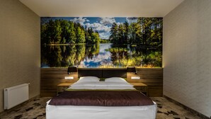 Un dormitorio con una cama grande, una mesita de noche, una lámpara de pared y vistas a un lago a través de una ventana.