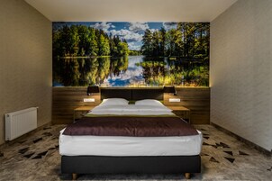 Un dormitorio con una cama grande, una mesita de noche, una lámpara de pared y vistas a un lago a través de una ventana.