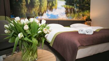 A hotel room with a bed, a vase of white tulips, and a painting of a lake.