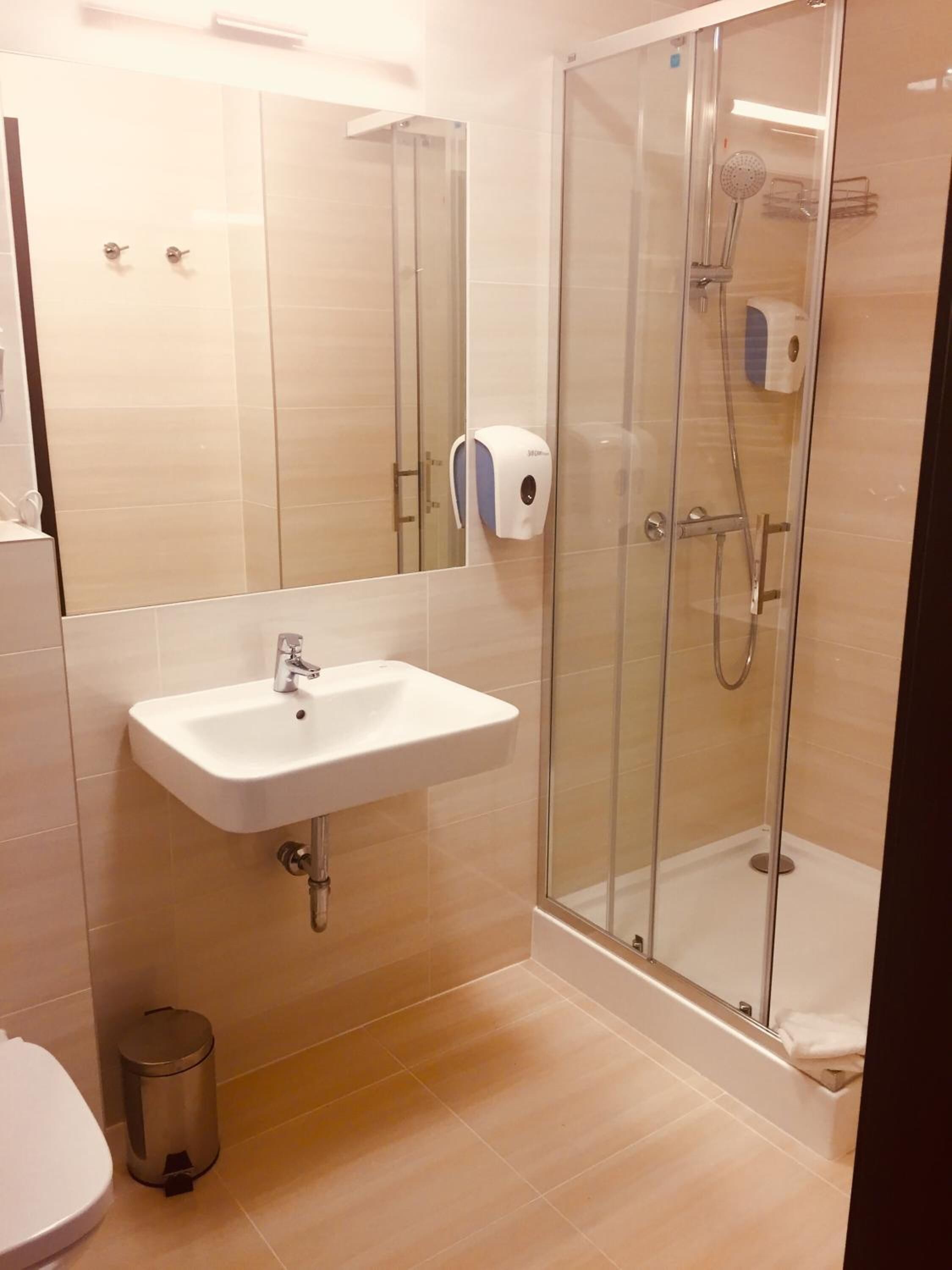 A modern bathroom with a glass-enclosed shower, a white sink, and a hand dryer.
