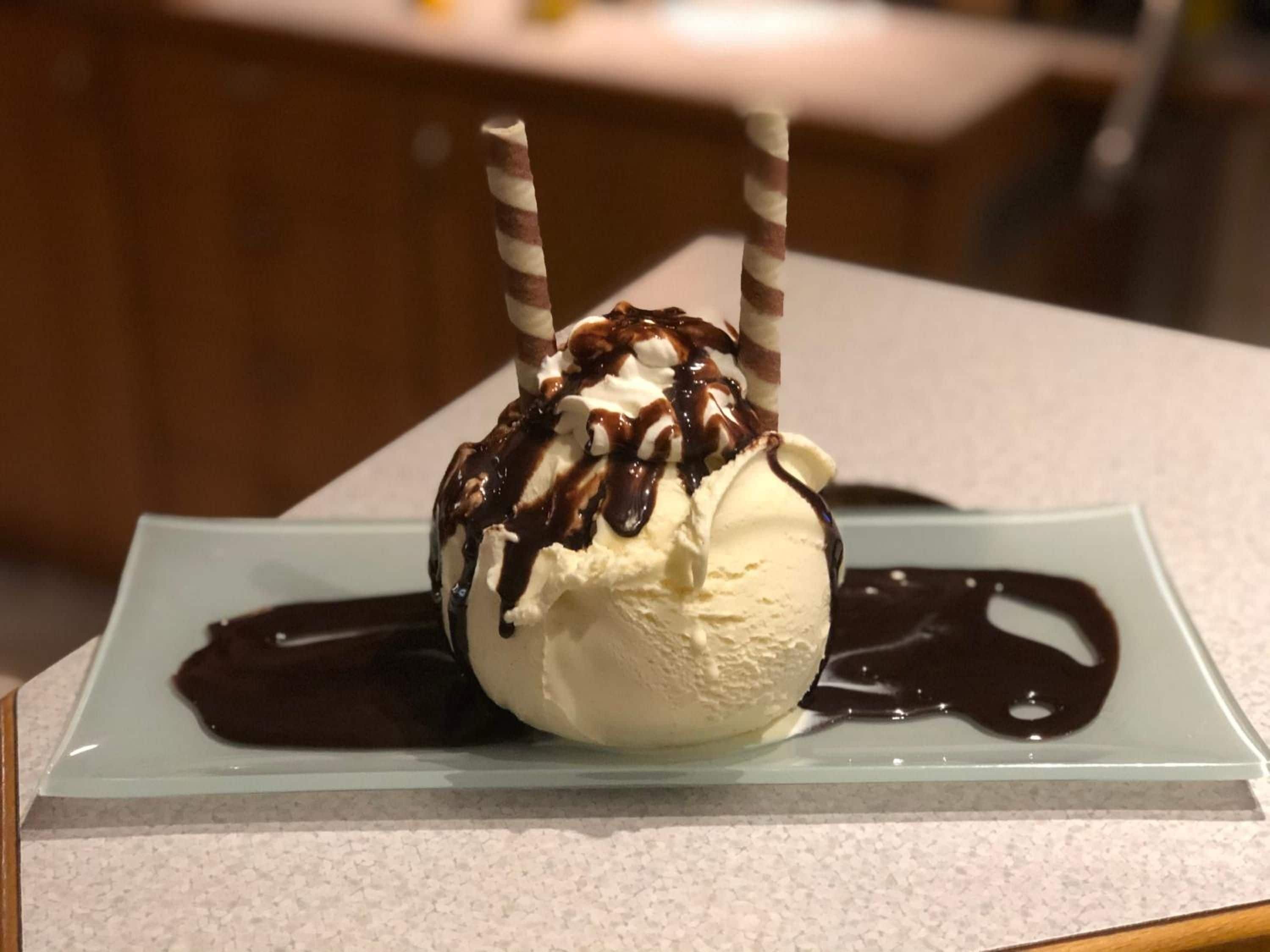 Ein Dessert auf einer Glasplatte mit Schokoladensauce und zwei gesstreiften Stäbchen.