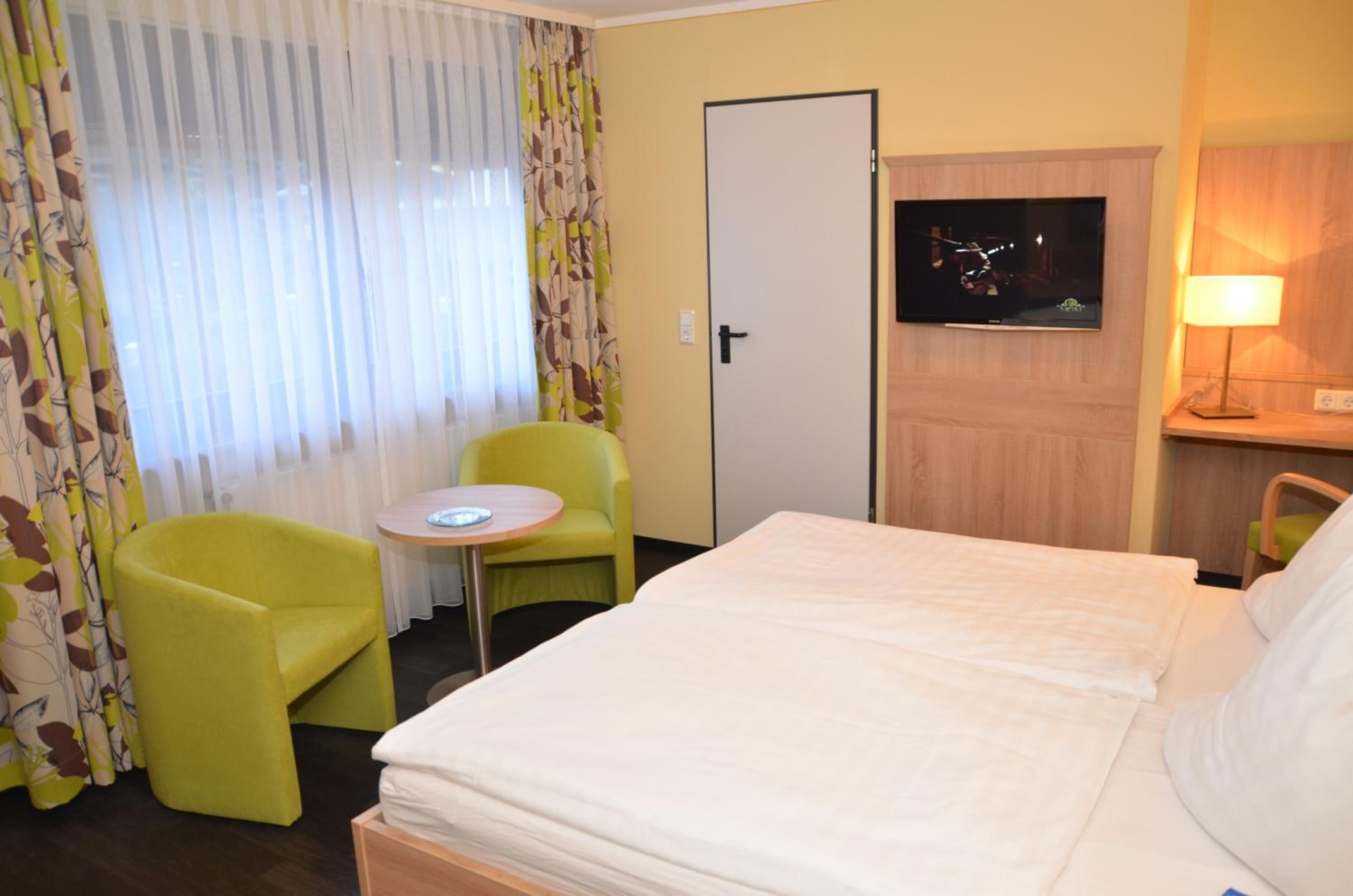 A hotel room with a bed, a small table, a chair, a television, and a lamp.
