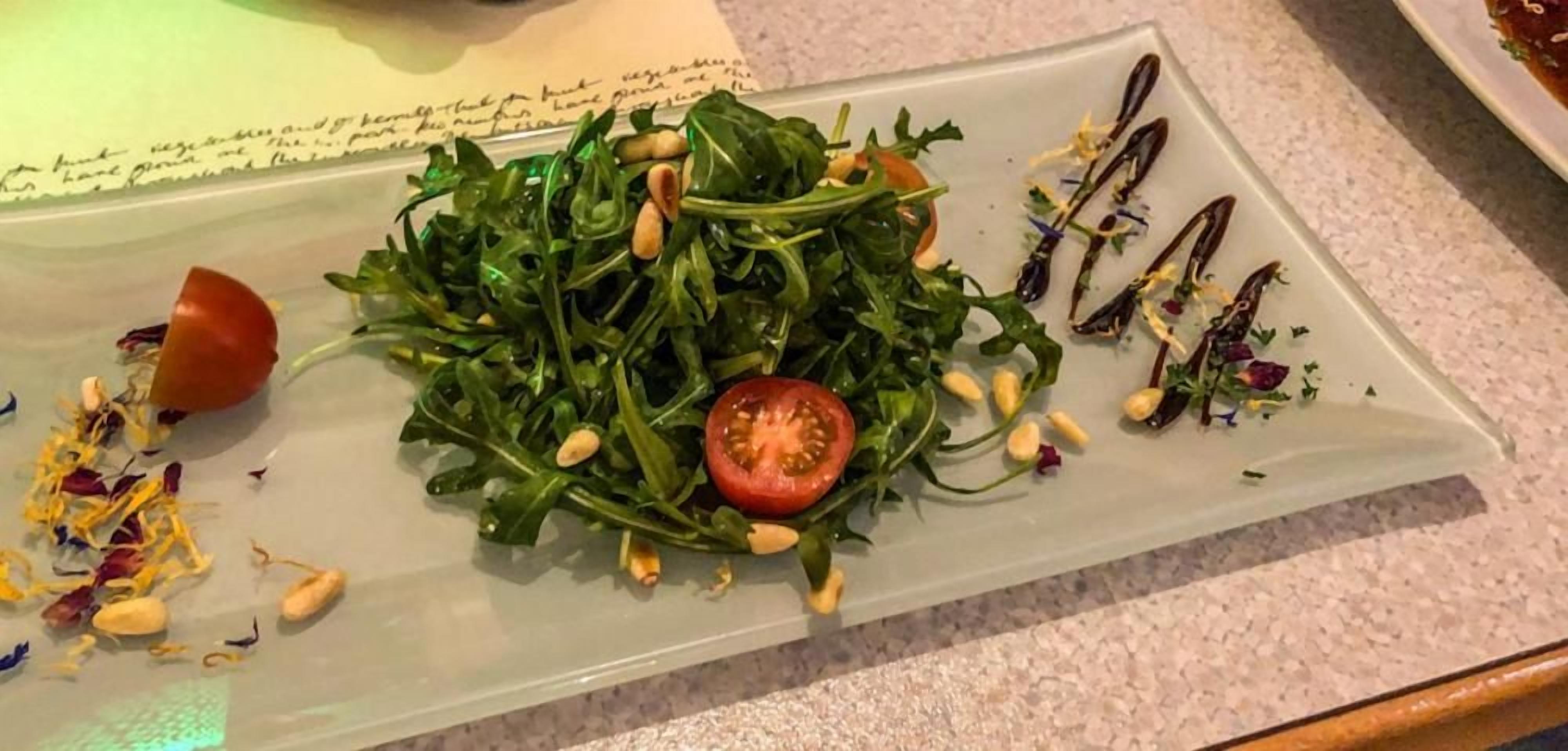 A plate of salad with greens, a tomato slice, and some nuts.