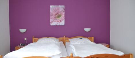 Una habitación con dos camas de madera, paredes moradas y un cuadro con una sola flor.