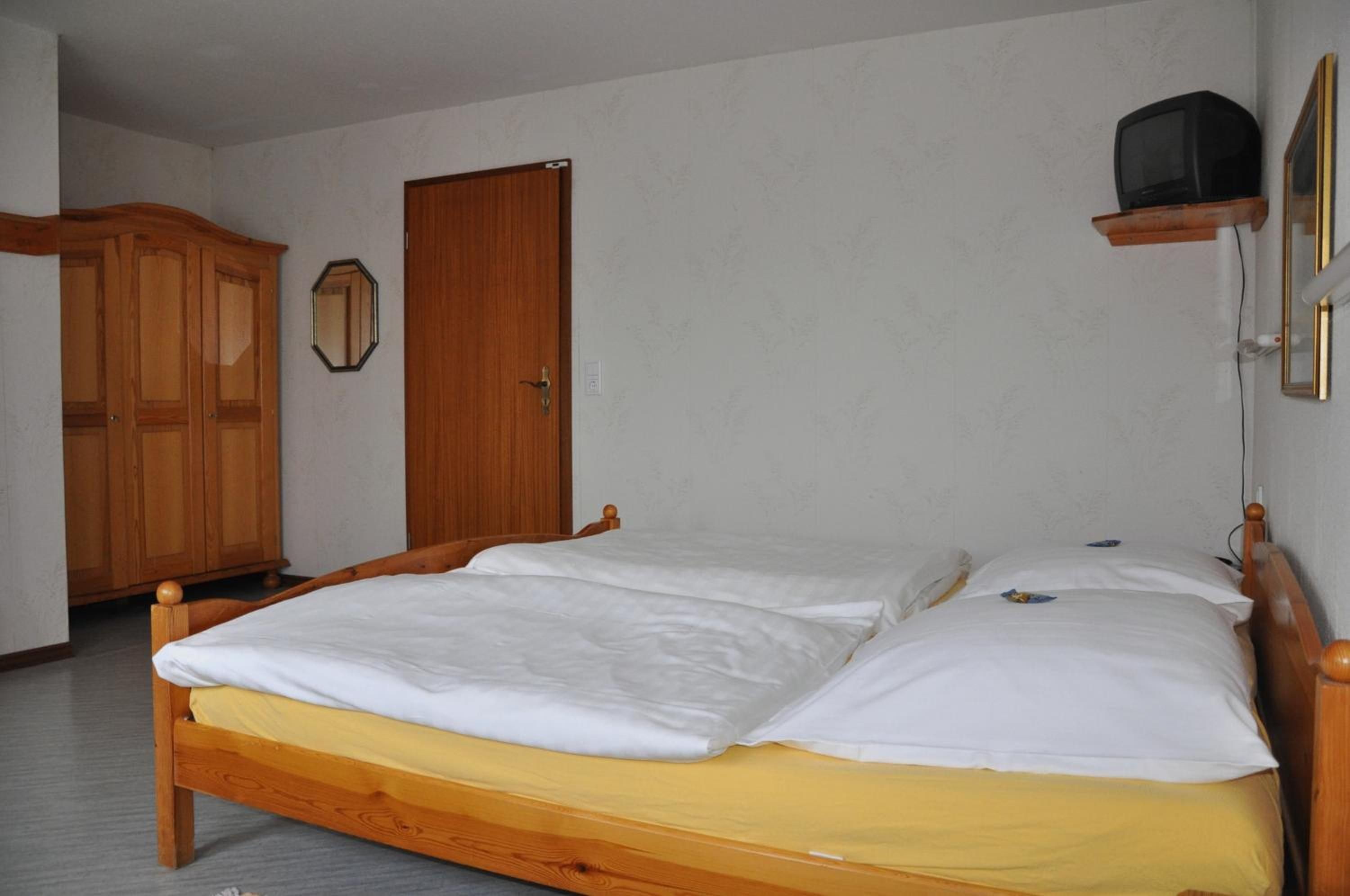 A bedroom with a wooden bed, a wardrobe, and a television on a shelf.