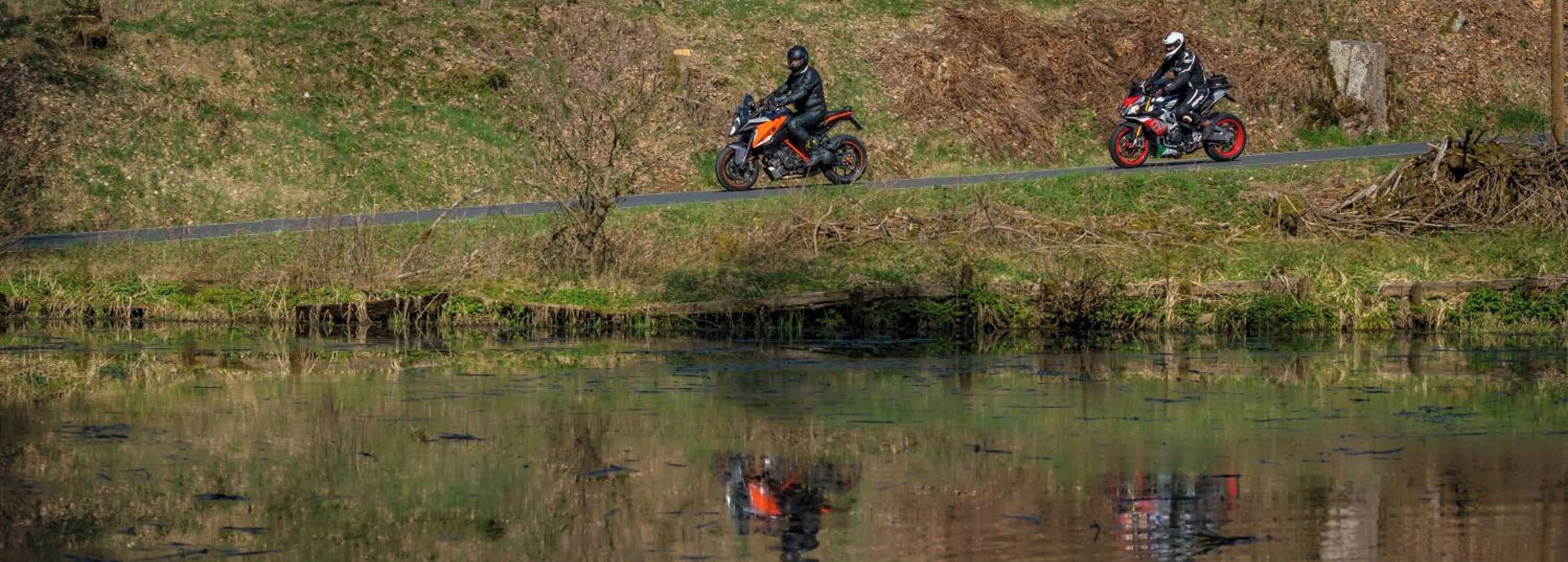 Dos motociclistas en una carretera con un cuerpo de agua al frente.