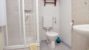 Un baño con ducha, inodoro, lavamanos y un estante con toallas.