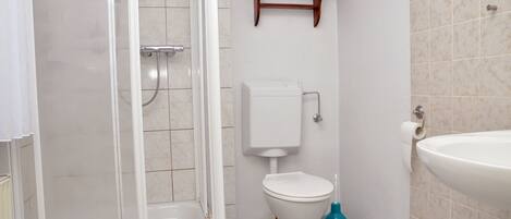 Un baño con ducha, inodoro, lavamanos y un estante con toallas.