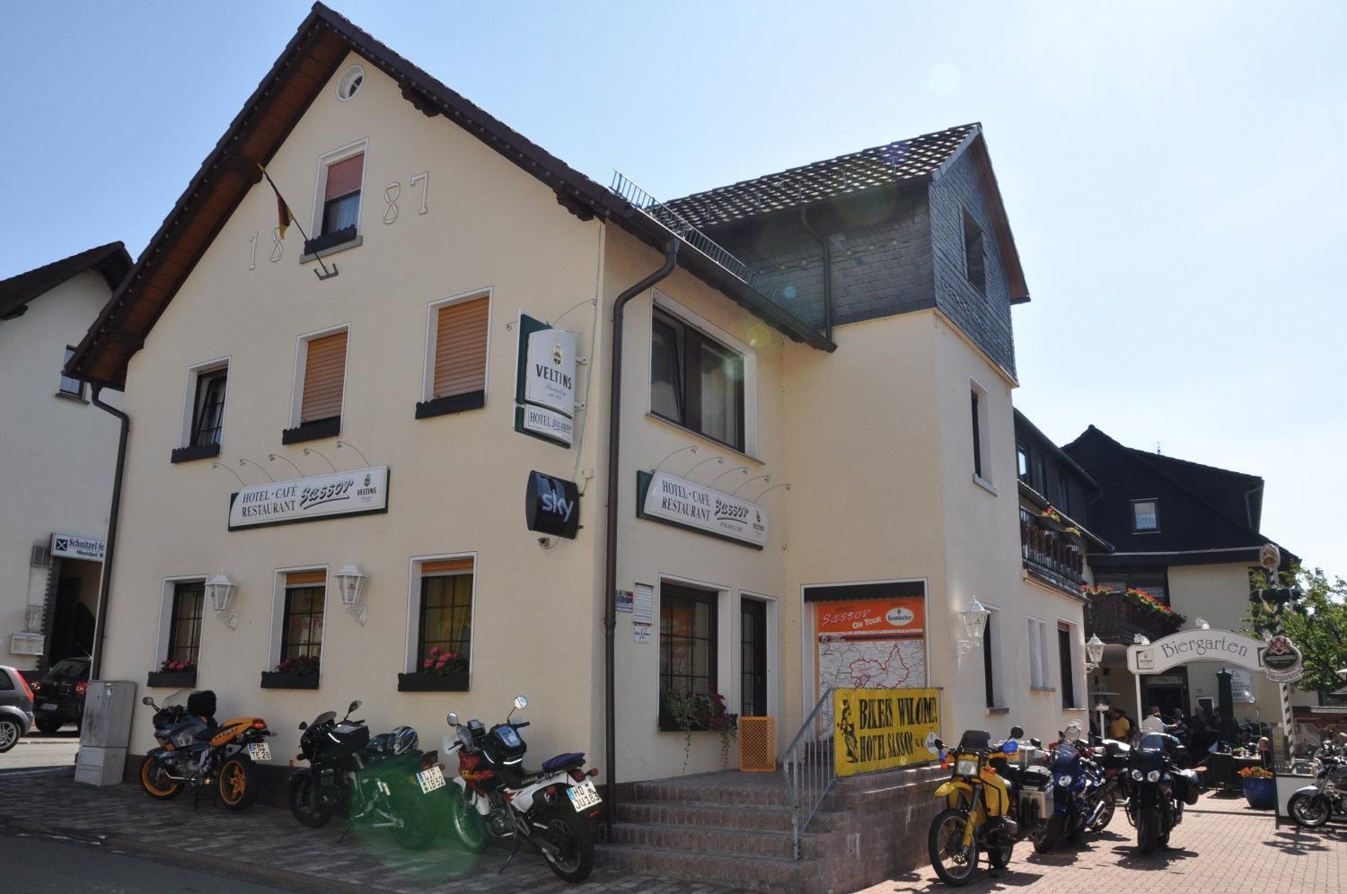 A building with multiple signs for a hotel, cafe, and restaurant. There are motorcycles parked in front.
