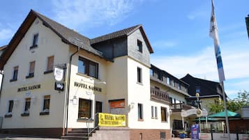 Een hotel met twee verdiepingen in traditionele Europese stijl, met een opvallende ingang en een wimpel.